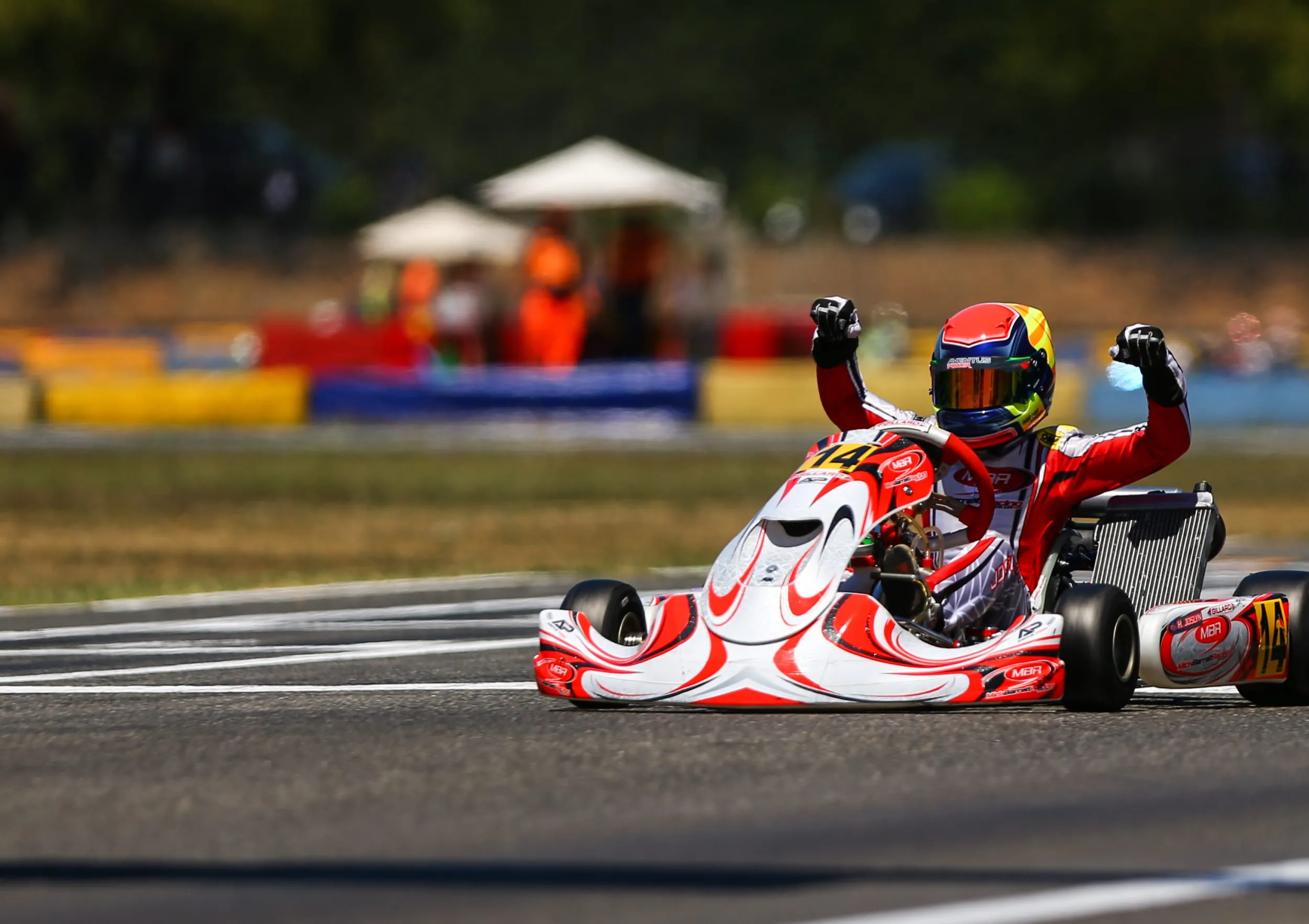 young kart driver with arms raised to celebrating a win on a motor racing circuit